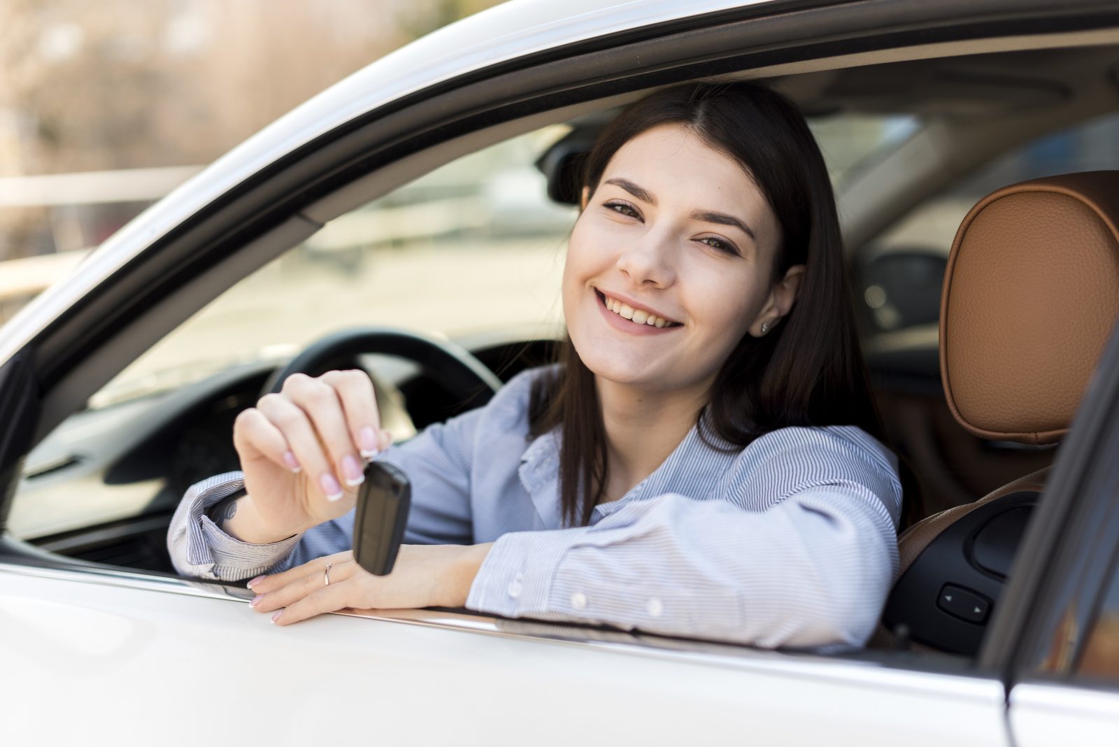smiling brunette young businesswoman inside car holding key out window